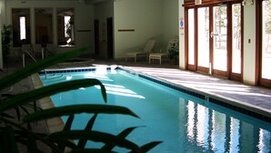 An indoor swimming pool with clear glass walls, a tiled floor, and several lounge chairs. - Pool, Hot Tub, Elevator, Gym! Walk to River Trail, Festivals, Dining, Shops (Keystone)