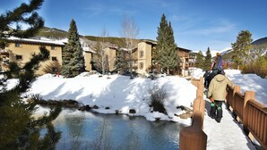 A wooden bridge over a partially frozen river with snow-covered banks and buildings in the background. - Pool, Hot Tub, Elevator, Gym! Walk to River Trail, Festivals, Dining, Shops (Keystone)