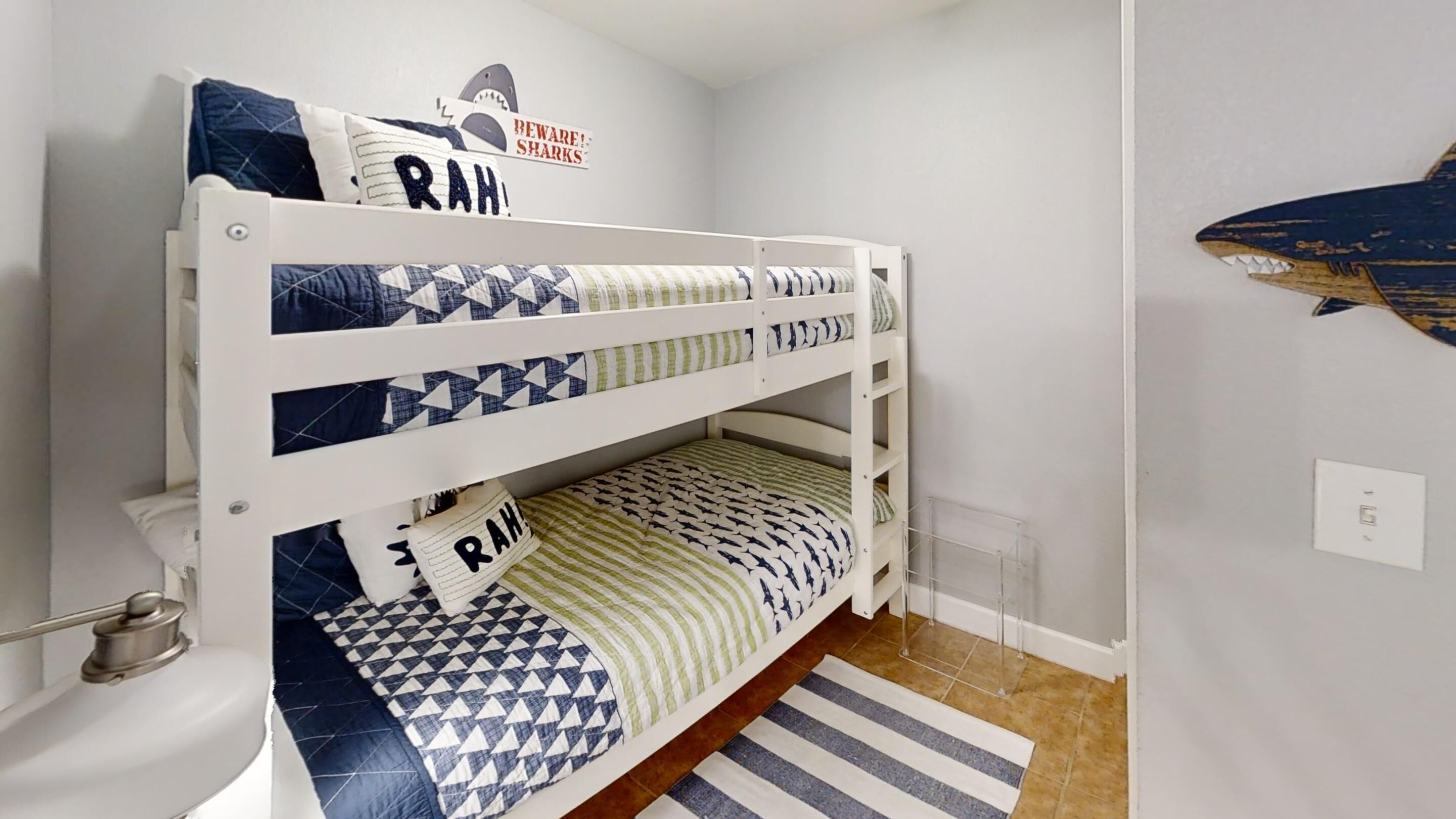 A bunk bed with geometric patterned bedding, a shark decoration on the wall, and a striped rug on the floor.