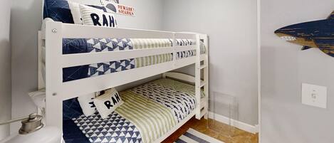 A bunk bed with geometric patterned bedding, a shark decoration on the wall, and a striped rug on the floor.