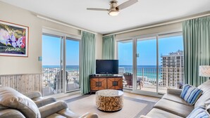 Un balcon spacieux offrant une vue sur l’océan, un téléviseur à écran plat et un coin salon confortable agrémenté d’un pouf à motifs.