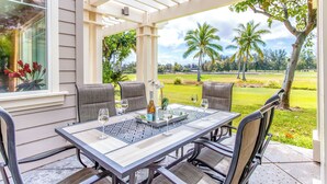An outdoor patio with a table set for two, surrounded by chairs, and a view of a golf course. - Comfortable Townhome in Waikoloa Resort - Walk to Shops! (Waikoloa)