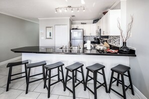A modern kitchen with a black countertop, white cabinets, and five black bar stools.