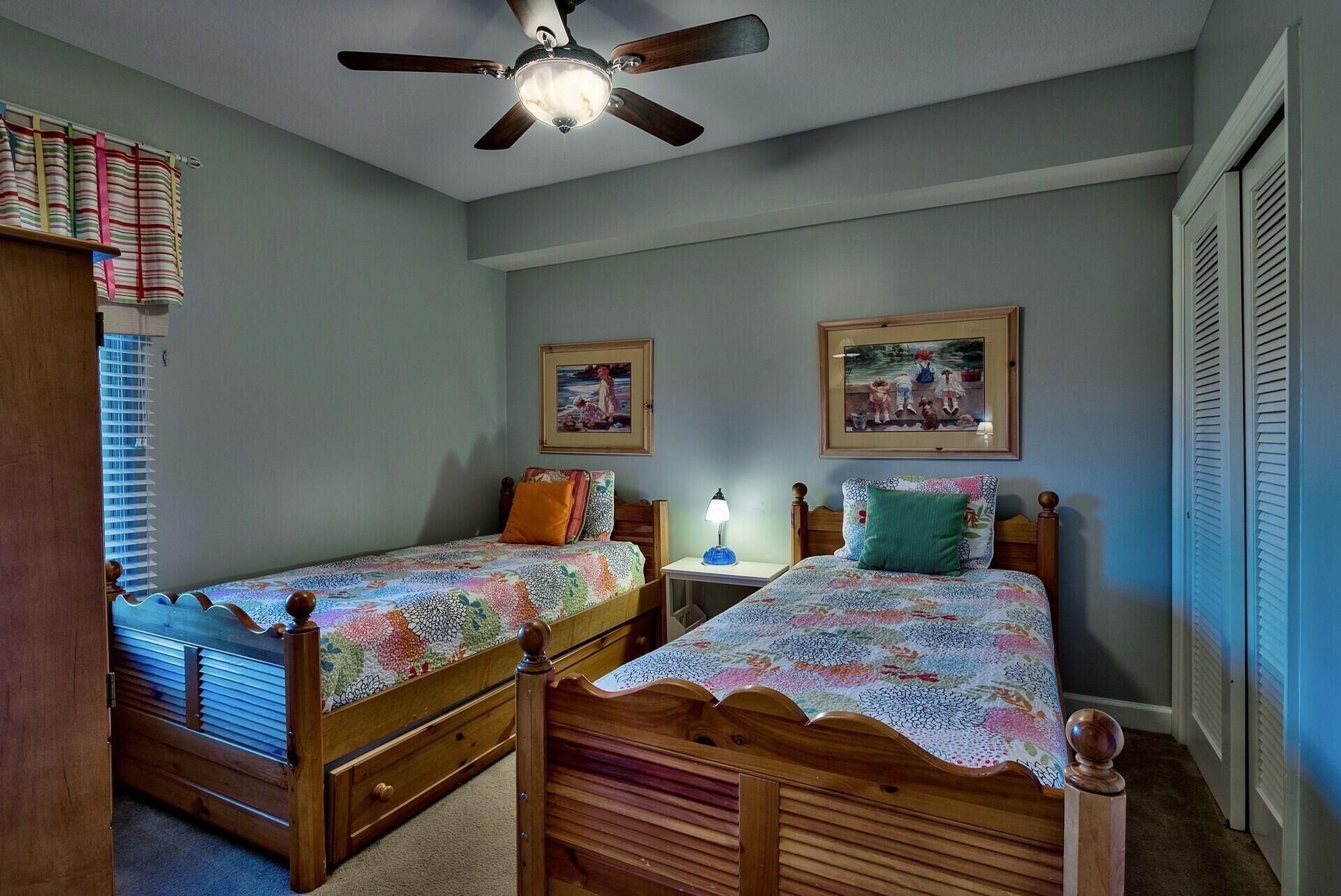 A bedroom with two wooden beds, a ceiling fan, and two framed pictures on the wall.