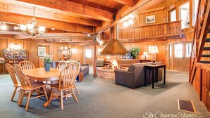 L’intérieur chaleureux du chalet comprend un coin repas en bois, une cheminée et un salon avec un canapé et une table.