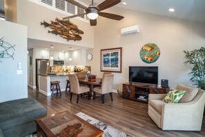 A modern living room with a dining area, a ceiling fan, a flat-screen TV, and a large plant.