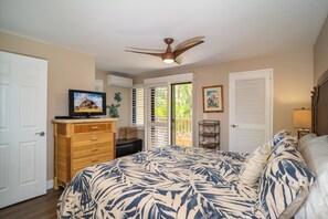 A bedroom with a bed, dresser, television, ceiling fan, and a door leading to a balcony.