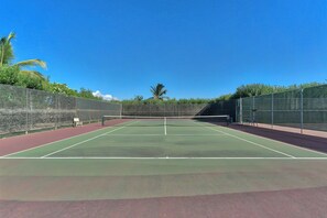 A tennis court with a net, surrounded by a fence and greenery.