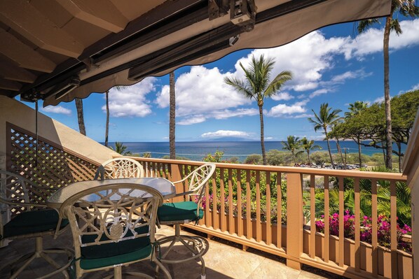 A balcony with a view of the ocean, palm trees, and a wooden railing.