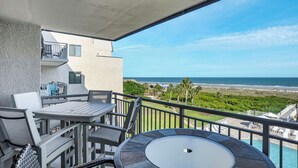 Ein Balkon mit Tisch und Stühlen mit Blick auf Strand und Meer.
