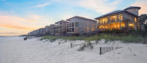 A beachfront property with multiple buildings, a sandy beach, and a wooden fence.