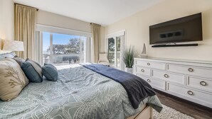 Un dormitorio con cama, tocador, televisión y vistas al exterior.
