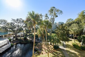 Stroll across the tranquil water feature to the lush surroundings, surrounded by palm trees and multi-story buildings.