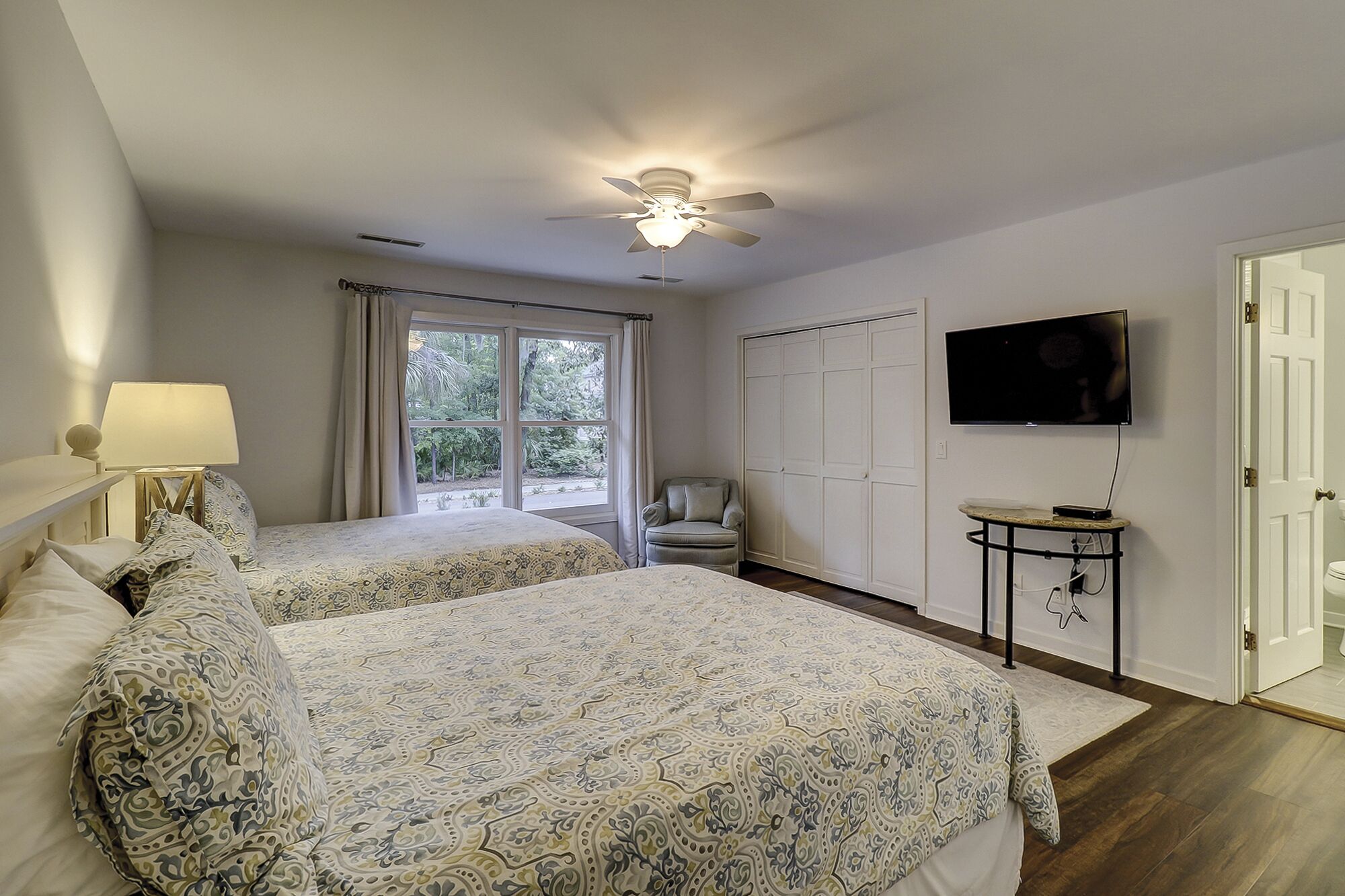 Un dormitorio con dos camas, ventilador de techo, televisor y ventana con cortinas.