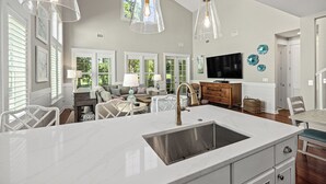 Una cocina con una isla grande, armarios blancos y un lavamanos de acero inoxidable integrado.