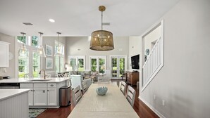 Una cocina moderna con armarios blancos, una isla central y un comedor con una mesa larga.