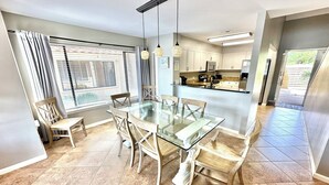 Una cocina moderna con una mesa de comedor de vidrio y sillas, horno empotrado y un ventanal con persianas.