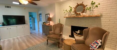 A living room with two armchairs, a patterned rug, a fireplace, and a television in the background.