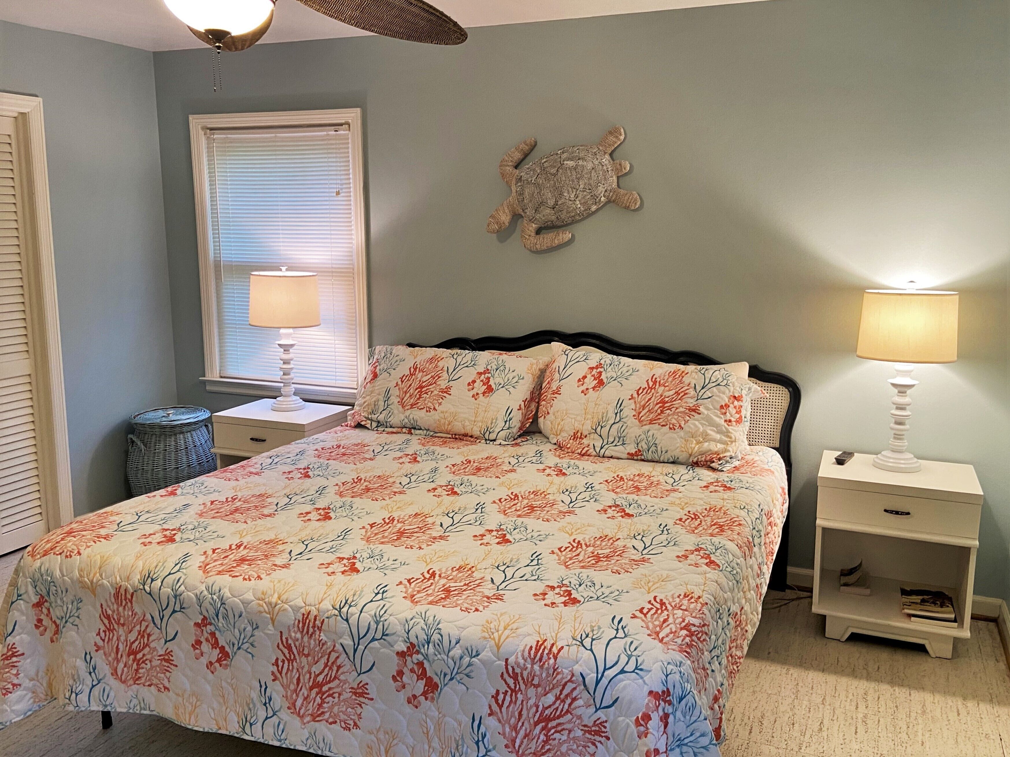 A bedroom with a bed, two nightstands, a ceiling fan, a window with blinds, and a wall decoration.