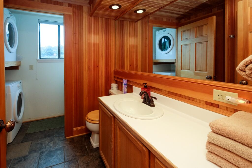Un baño con paneles de madera, un lavamanos, un espejo y dos lavadoras.