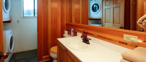 Un baño con paneles de madera, un lavamanos, un espejo y dos lavadoras.