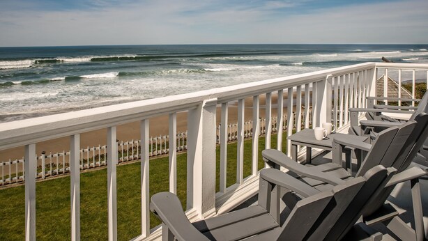 Een balkon met uitzicht op de oceaan, een witte reling en diverse lounge fauteuils.