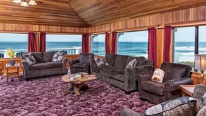 Een gezellige woonkamer met houten balkenplafond en grote ramen met uitzicht op de oceaan.