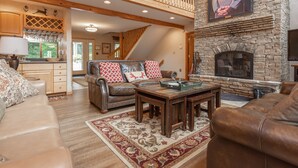 A spacious living room with a stone fireplace, leather sofas, and a wooden coffee table. - Dog Friendly Lakefront Retreat w/ Pool & Hot Tub (McHenry)