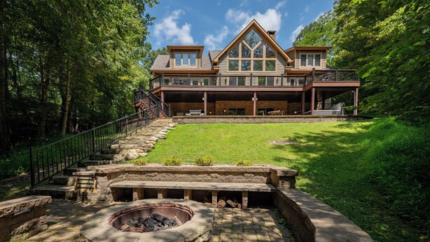 A large, two-story house with a stone fire pit in the front yard. - Dog Friendly Lakefront Retreat w/ Pool & Hot Tub (McHenry)