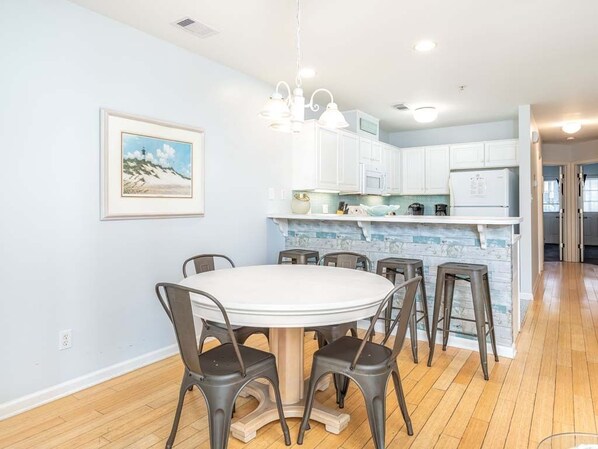 A modern kitchen with white cabinets, a central island, and a dining area with a round table and chairs.
