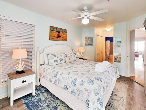 A bedroom with a bed, two bedside tables, a ceiling fan, and a window with blinds.