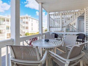 A covered outdoor seating area with wicker chairs and a round table, overlooking a residential building with balconies. - South Beach Ocean 4 | Condo, Partial Ocean View! (Tybee Island)