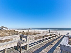 A wooden boardwalk leading to a beach with a pier in the background. - South Beach Ocean 4 | Condo, Partial Ocean View! (Tybee Island)