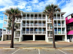 A multi-story hotel with balconies, a covered parking area, and palm trees. - South Beach Ocean 4 | Condo, Partial Ocean View! (Tybee Island)