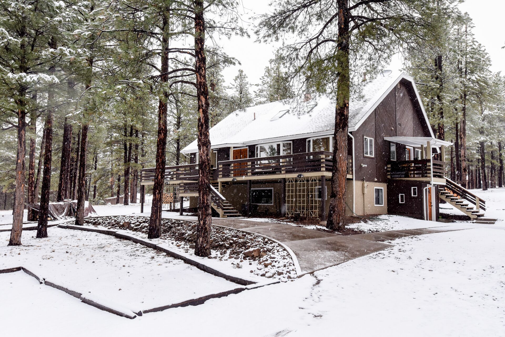 Eine große Holzhütte mit mehreren Ebenen, umgeben von hohen Kiefern und bedeckt mit Schnee.