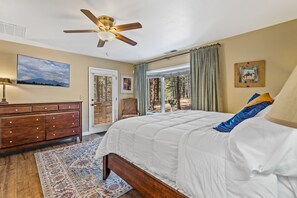 Un dormitorio con cama, ventilador de techo, cómoda, alfombra y ventana con cortinas.