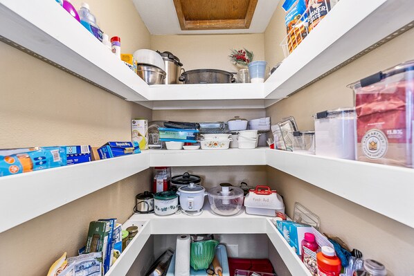 Una despensa bien organizada con estantes llenos de alimentos, utensilios de cocina y recipientes de almacenamiento.
