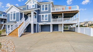 A two-story house with a covered front porch and a staircase leading to the upper level. - SEMI Oceanfront!  Beautiful decor, ocean vws! Noon check in! Pool, HotTub (Corolla)