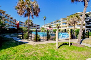 A hotel with multiple balconies, a swimming pool, and palm trees. - Cozy, waterfront condo with hot tubs, pools, tennis court, and fitness room (Galveston)