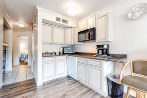 A modern kitchen with white cabinetry, a microwave, a coffee maker, and a trash can. - Cozy, waterfront condo with hot tubs, pools, tennis court, and fitness room (Galveston)