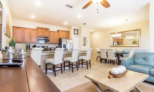 A modern kitchen with wooden cabinets, a dining area with white chairs, and a blue sofa.