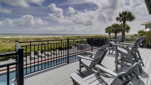 Une terrasse avec des chaises longues donnant sur une piscine et une plage.