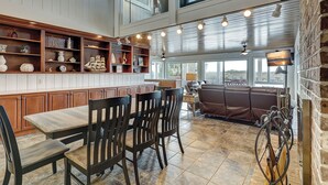 Une salle à manger aux hauts plafonds, dotée de meubles en bois et offrant une vue sur l’extérieur.