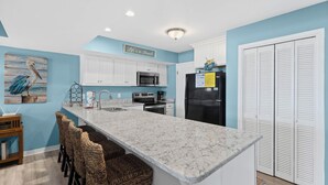 A kitchen with white cabinets, a marble countertop, and a sign that reads 'It's a Beach.' - Unit 032 - Sandcastle 5B (Dauphin  Island)