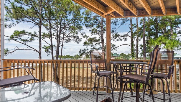 A covered outdoor deck with wooden railings, metal chairs, and a glass table. - Unit 032 - Sandcastle 5B (Dauphin  Island)