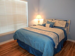A bedroom with a bed, a nightstand with a lamp, and a window with blinds. - Gulf View Home on the Beautiful West End of Dauphin Island (Dauphin Island)