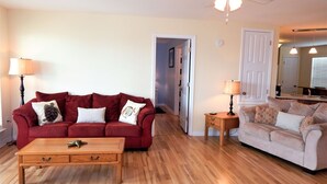 A living room with a red sofa, a white sofa, a wooden coffee table, and a ceiling fan.