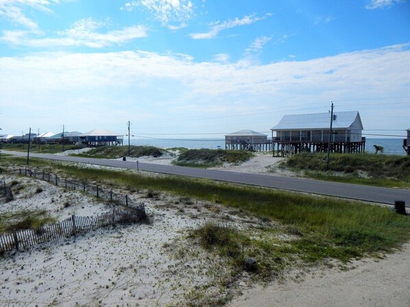 A coastal road with sandy dunes and beach houses on stilts.