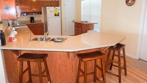 A kitchen with wooden cabinets, a white refrigerator, a sink, and two bar stools.