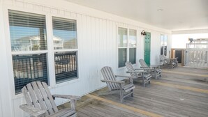 A covered porch with wooden deck and Adirondack chairs.